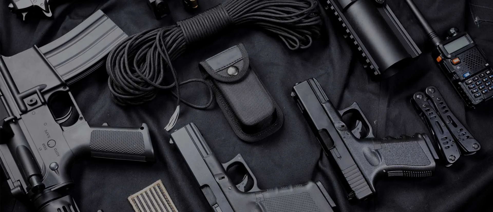 Flat-lay of tactical shooting gear: rifle, semi-automatic pistols, magazine, radio and multi-tool