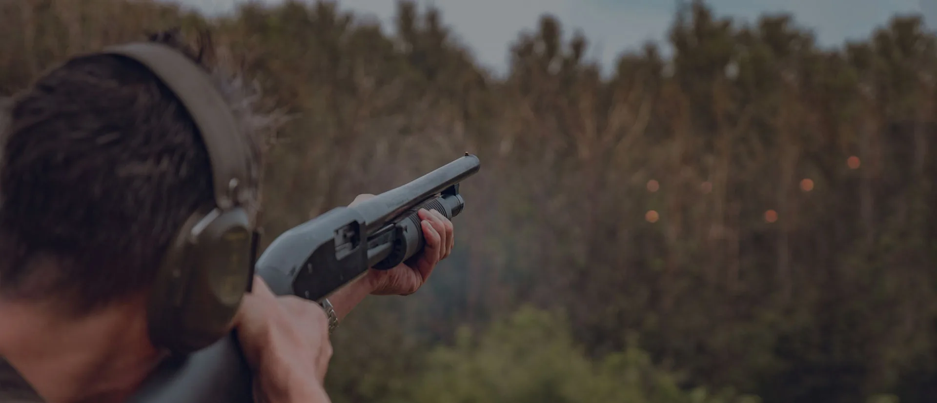 Shooter aiming a shotgun with ear protection during sporting clays training at an outdoor range in New York