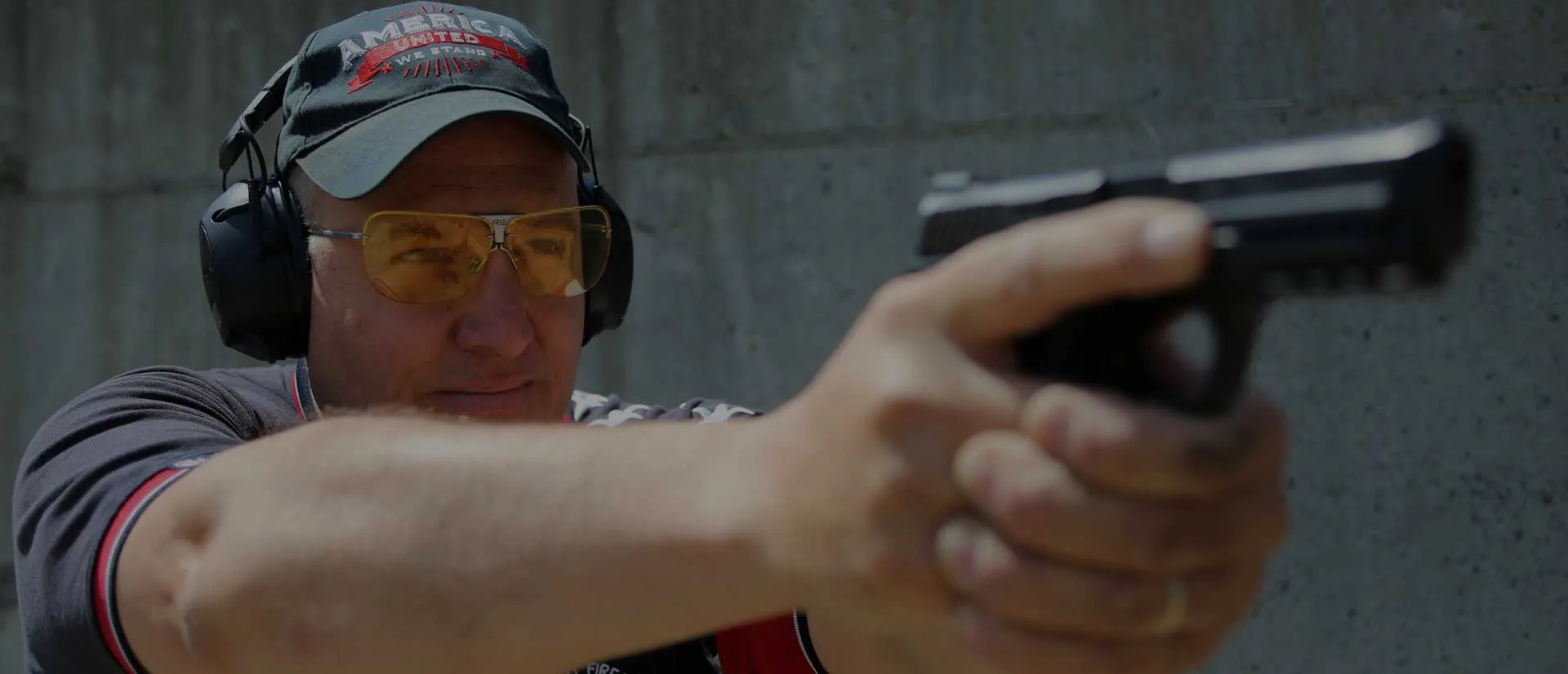 Man aiming a semi-automatic handgun with safety gear at an outdoor shooting range